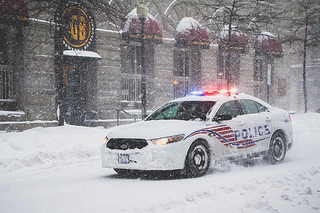A District of Columbia Police car drives through heavy snow with emergency lights flashing on 9th street in Washington DC during Blizzard 2016.