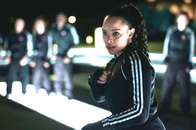 Rose Hathaway from the TV show Vampire Academy wearing a black training suit and holding her hands up in a guarding position, ready to fight.