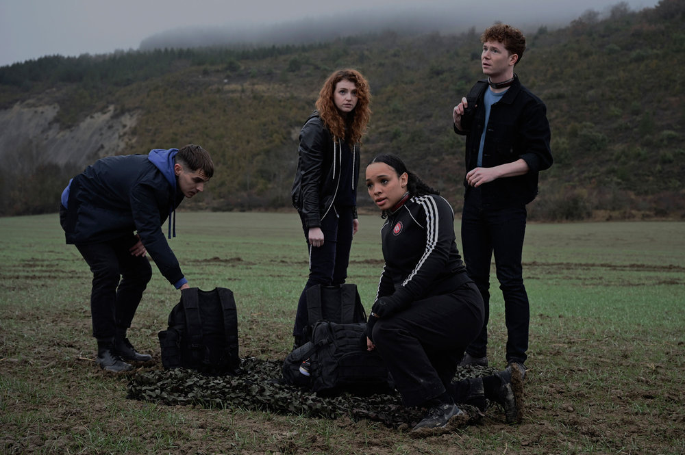 The dhampirs from Vampire Academy gathered in black with backpacks, ready for a lesson in protecting their charge, who is standing next to them.