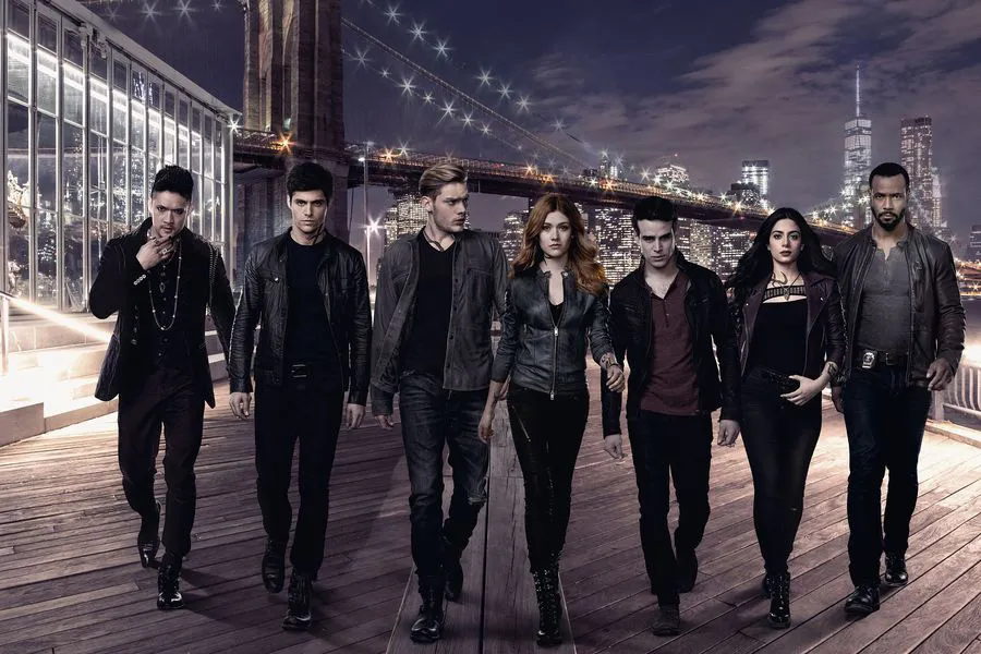 Shadowhunters cast wearing black and walking toward the camera. Left to right is Magnus, Alec, Jace, Clary, Simon, Isabelle, and Luke.
