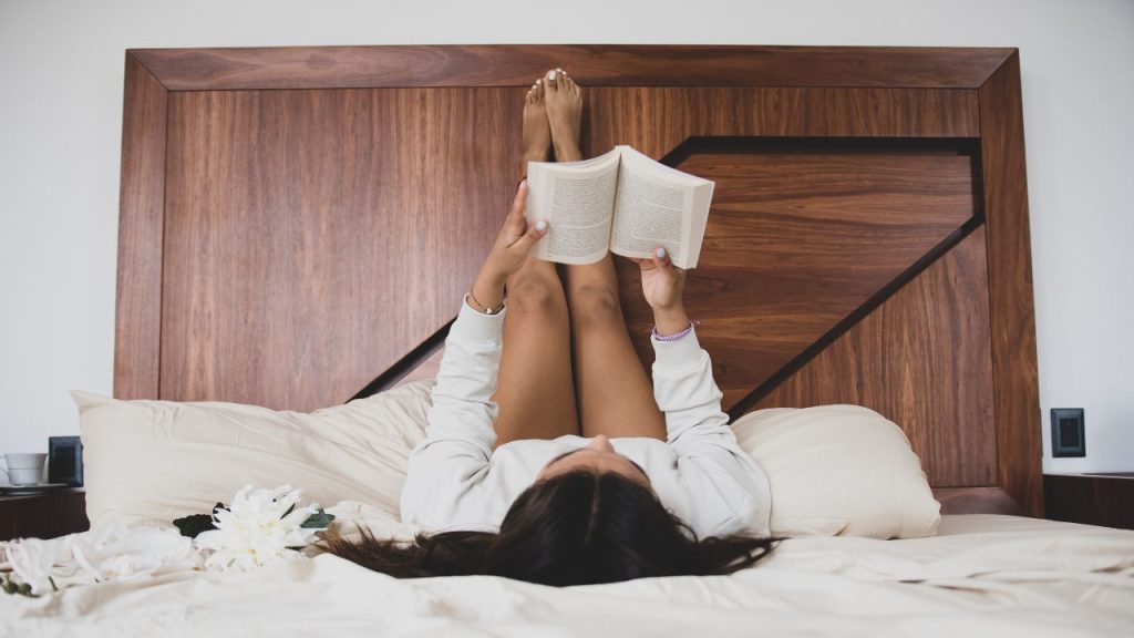 woman reading in bed with her legs up against her headboard