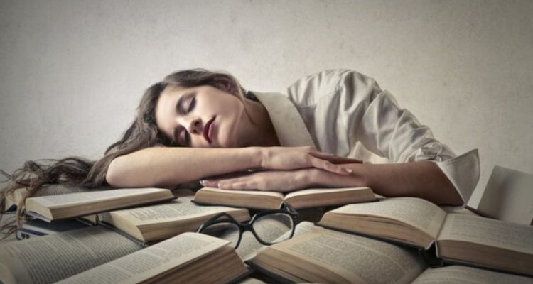 A woman sleeping on a bunch of books with black glasses on top of them