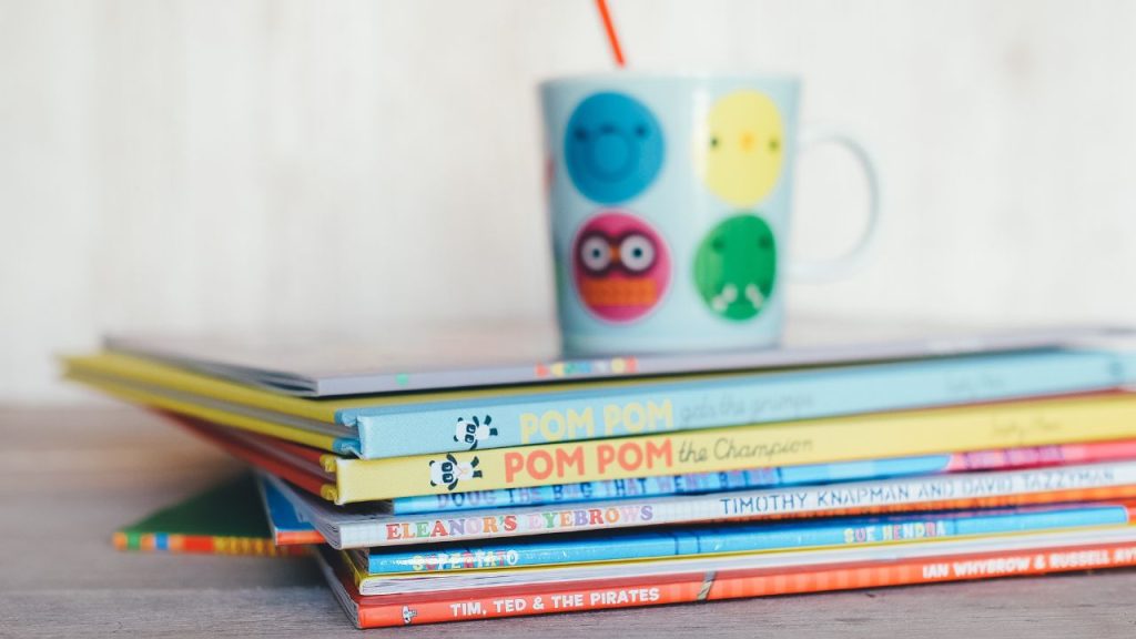 image showing a pile of children's books with a colorful mug sitting on top.