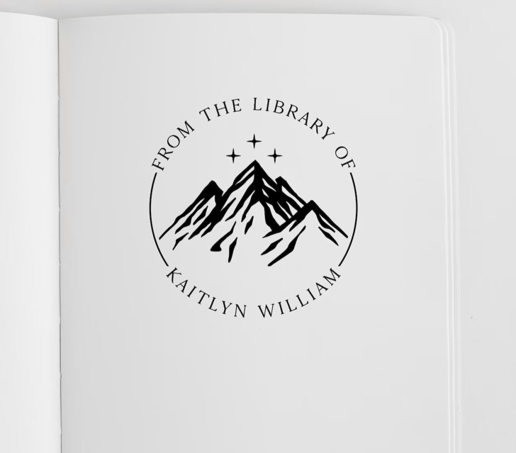 A black stamp saying "From the library of Kaitlyn William"; with three stars above mountains in the middle of the stamp that is stamped on white paper