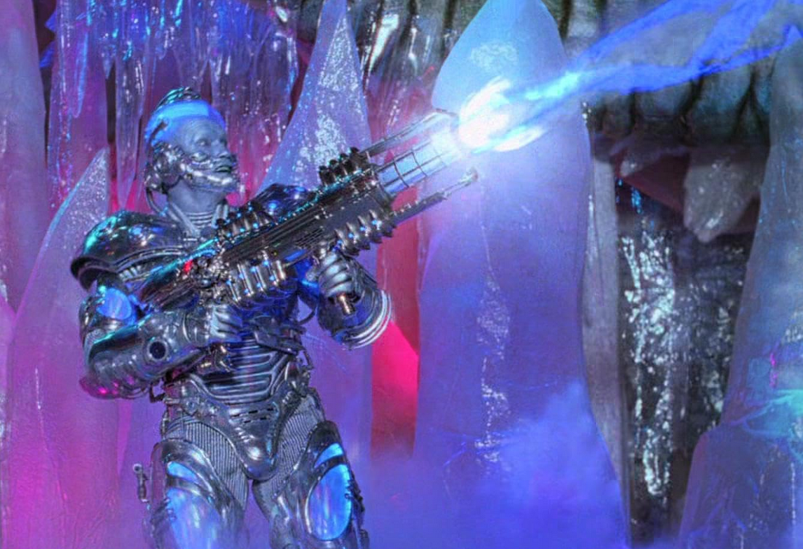 Mr. Freeze shooting is freeze gun with a happy expression on his face. His metal armor shines from the light off the gun. Large ice shards decorate the room behind him.
