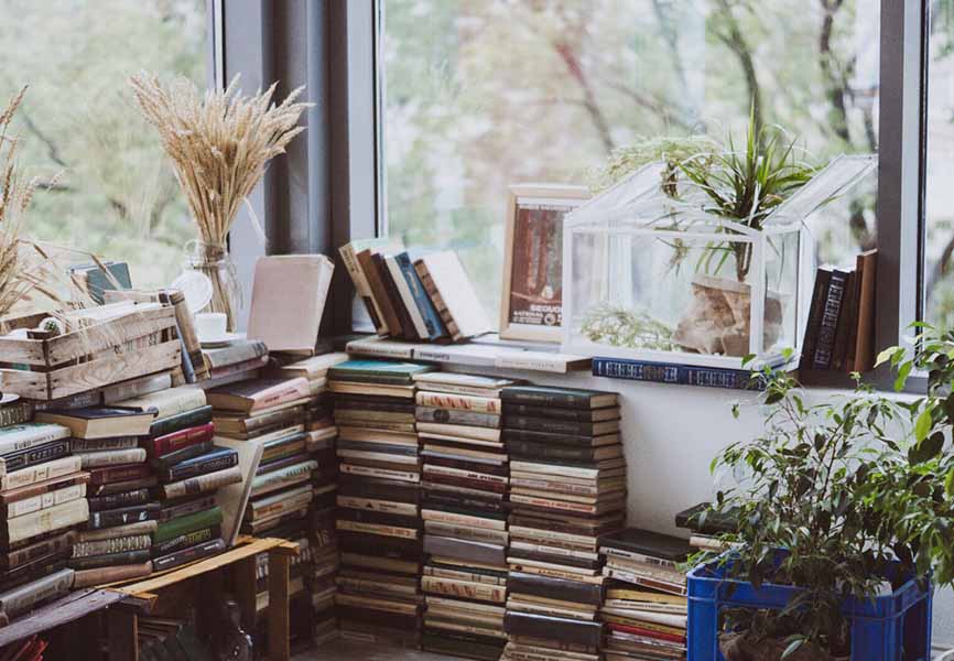 Books piled and lined up against a wall underneath a window