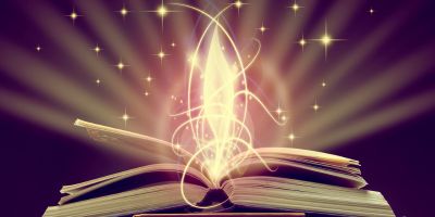 An open book with a golden flame dancing up from the book's pages. Golden strings swirl around the flame and open book. Gold sparkles twinkle around the book. Gold light emits from the book in a number of rays. The background is dark against the light, sparkles, and flame. Pages lift up from the book on the left and right side.