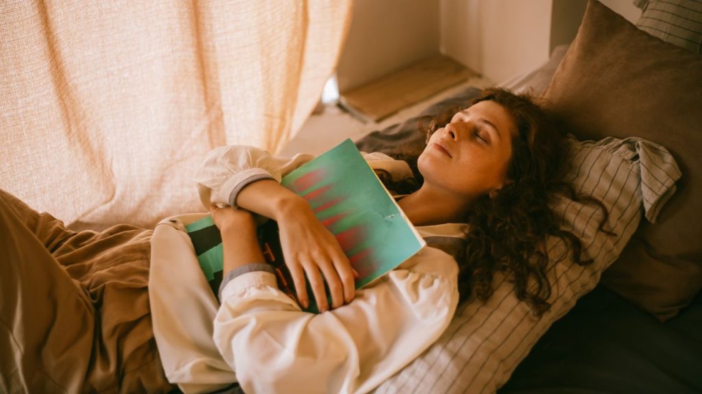 woman laying on a bed with her eyes closed hugging a book to her chest