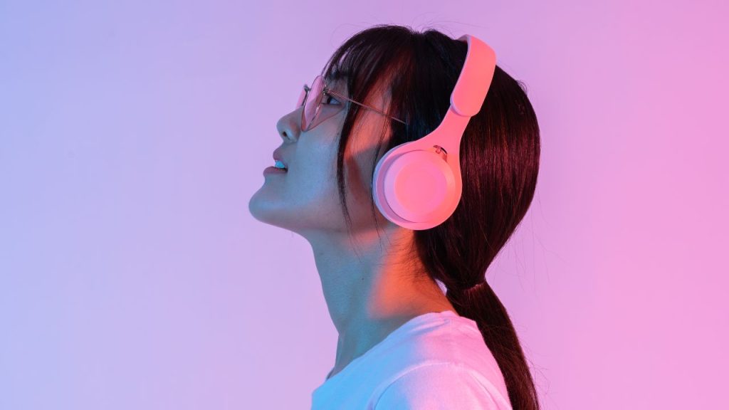 woman wearing headphones, background fades from purple to pink