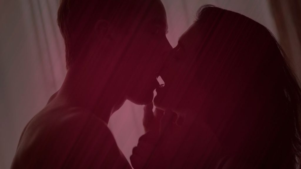 man and woman kissing intimately behand a sheet darkened foreground