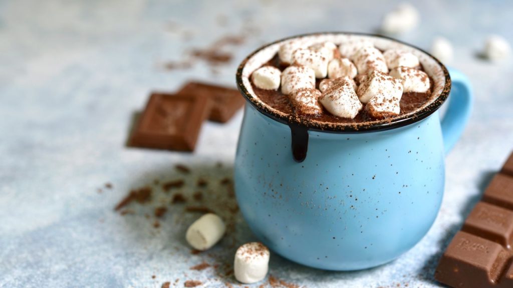 A blue mug of hot chocolate with marshmallows in it surrounding by pieces of chocolate. 