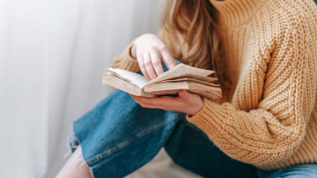 Woman wearing a yellow sweater reading a weathered book.