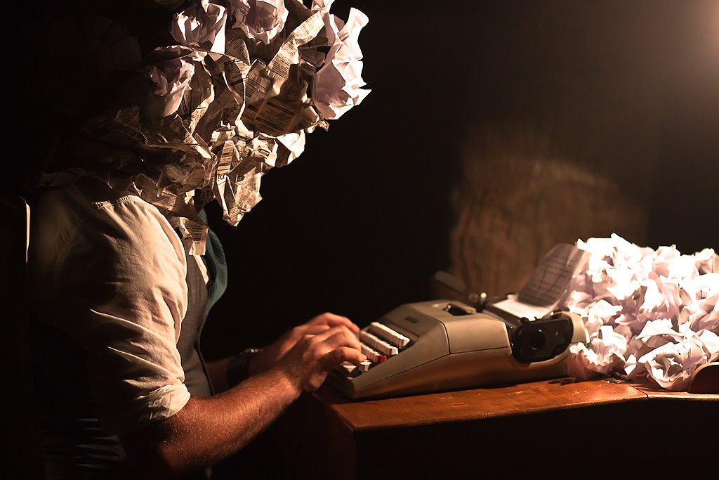 Person typing on a typewriter. Head is made of crumbled paper and crumbled paper is coming out of the typewriter.