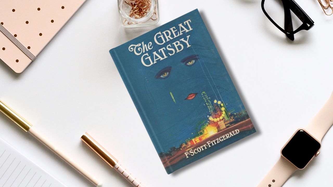 A Cover of the great Gatsby on a desktop with supplies and a watch