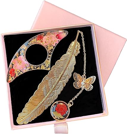 There's feathered bookmark with a gold chain and butterfly hooked to it. There's also a red flower pendant at the end of the chain. A butterfly shaped book/thumb page holder sits to the left of the feather bookmark. the feather is gold, and the book holder is different shades of pink and red. They are sitting in nice box with black inlay.