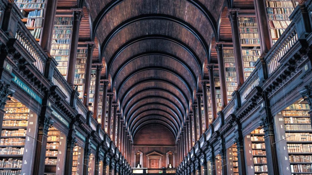 An upward image of a center aisle in a library, catching rows of filled bookcases on two floor levels.