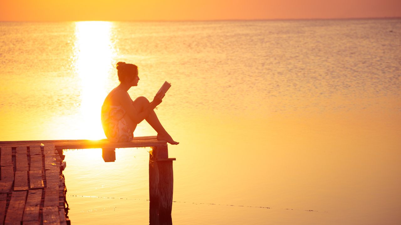 woman enjoying a book in the sunset on a dock.