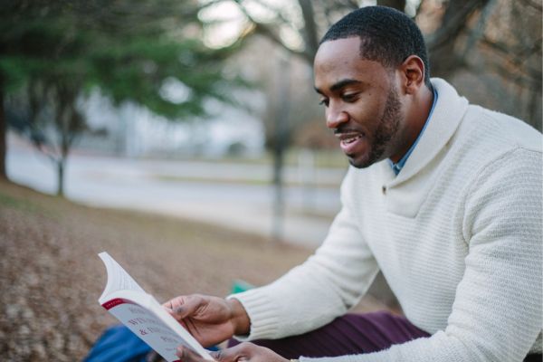 man reading a book in the fall outdoors.