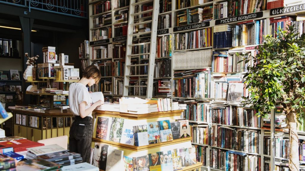 A woman reading in a bookstore with a ladder and tall shelves full of books.