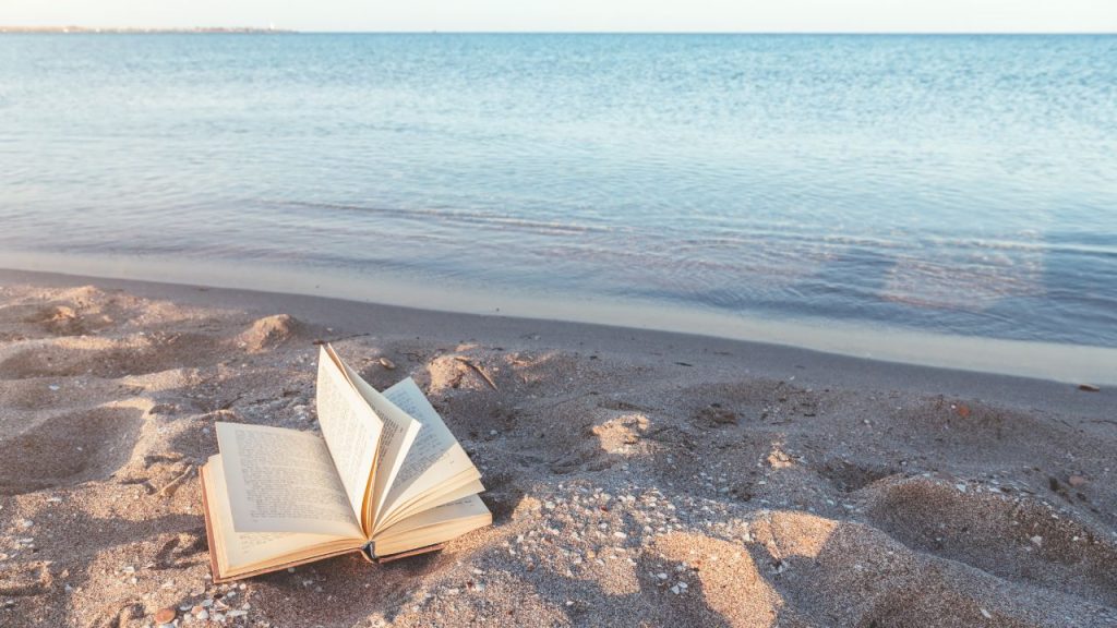 an open book with pages fluttering in the wind on a bright sandy beach.