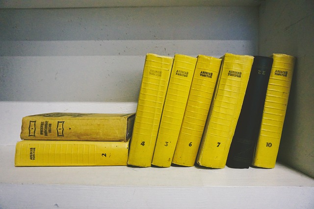 Yellow books stacked next to each other on a white shelf. There is one black book in the middle of the yellow ones.