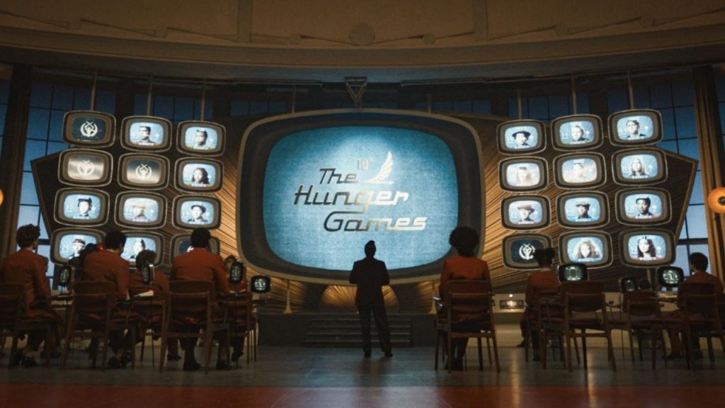 Image of the live viewing room for the 10th annual Hunger Games, showing a large screen with smaller screens of the tributes.
