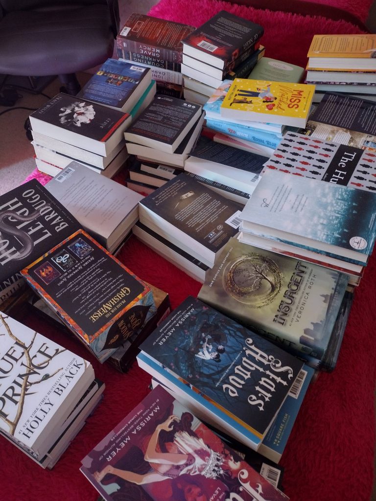 Several piles of books set on top of a pink bedspread.