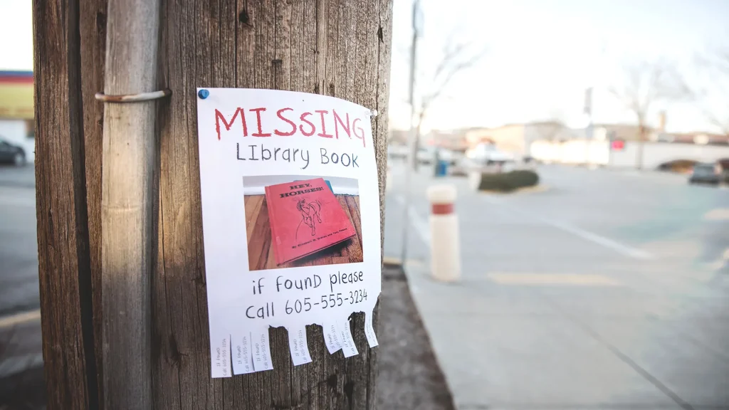 Light post with flyer depicting red missing library book with tear away phone numbers at the bottom