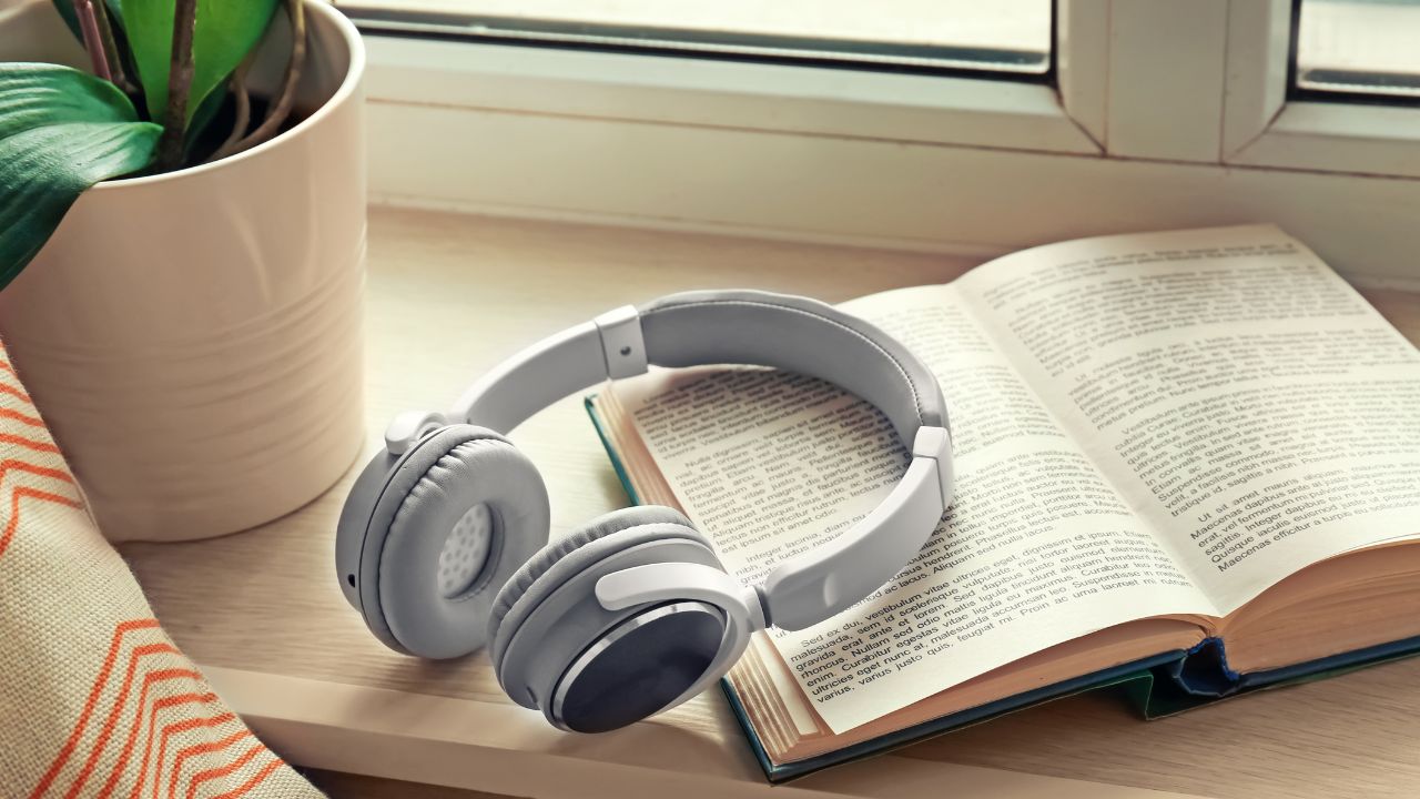 A pair of headphones resting on an open book resting on a windowsill next to a potted plant