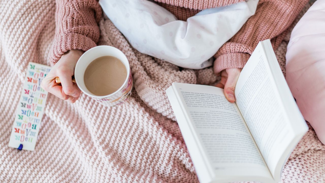 woman reading while drinking coffee in a cozy blanket.