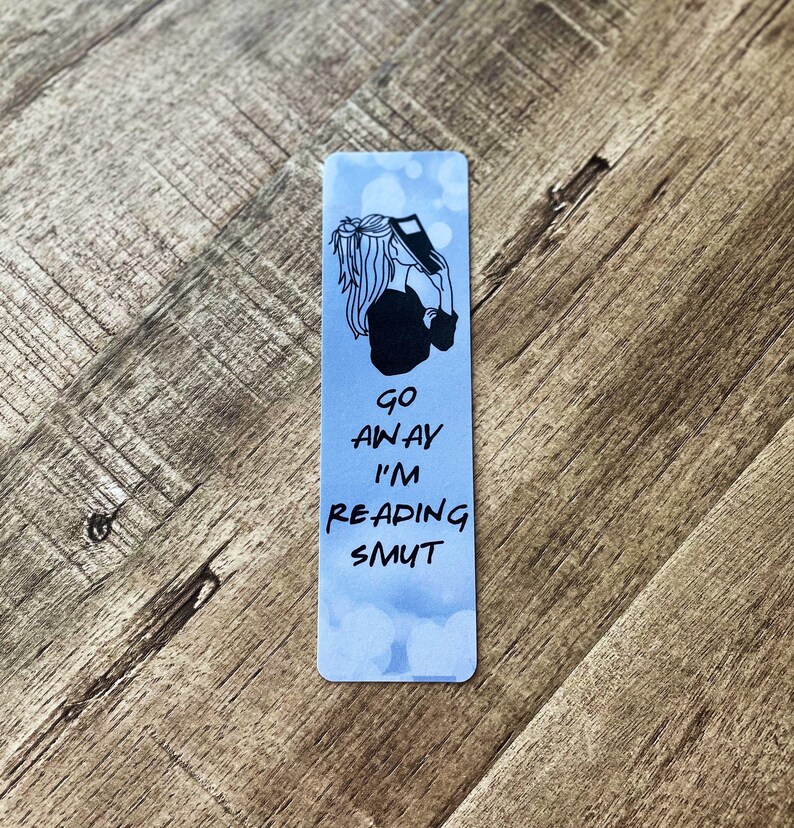 A blue cloud bookmark with someone covering their face with a book and the bottom says "Go away I'm reading smut"