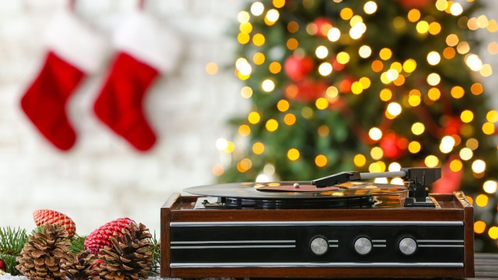 Image of a record player with Christmas decorations around it, and a Christmas tree in the background.