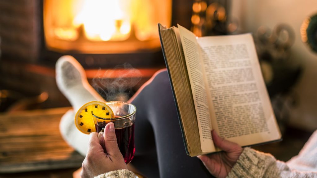 Image showing someone sitting by a fire with a book and a hot drink in hand. 