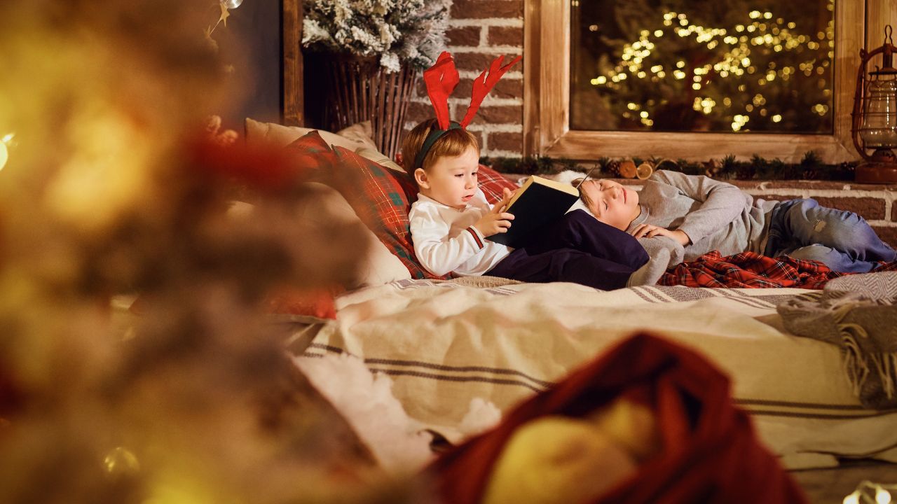 young child reading a book before a christmas tree