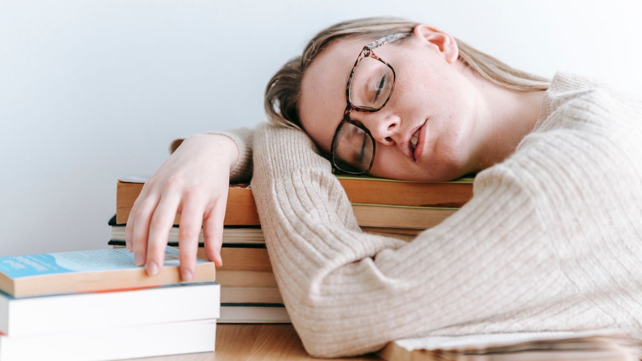 A woman wearing glasses sleeping on a pile of books