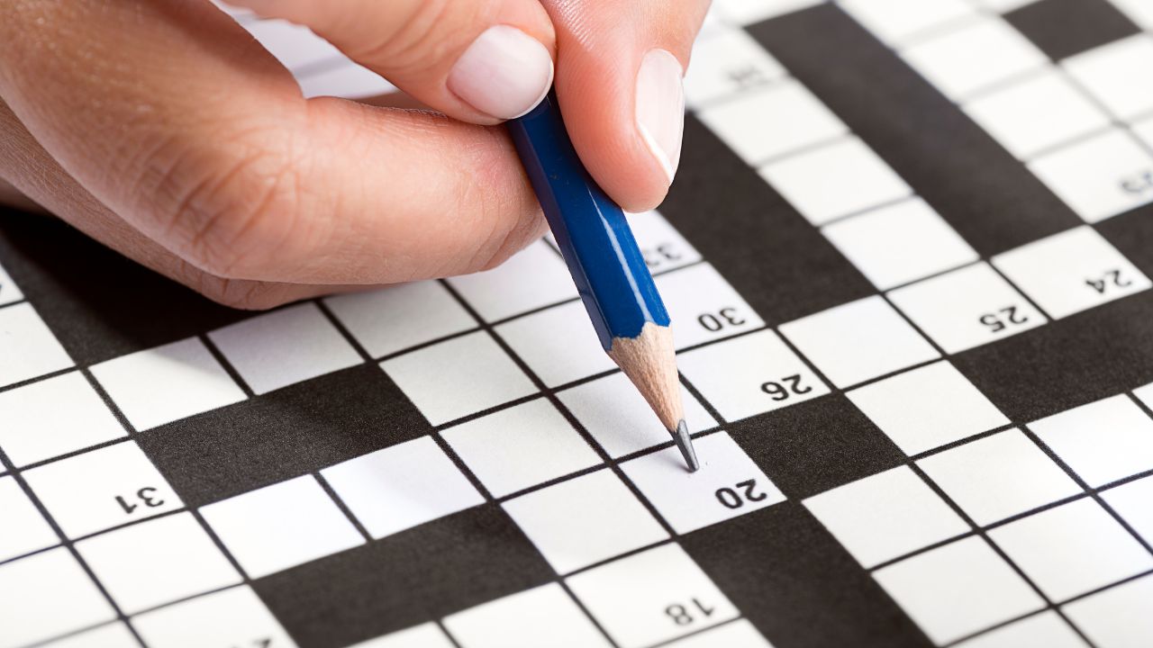 Someone filling out a crossword puzzle with a blue pencil.