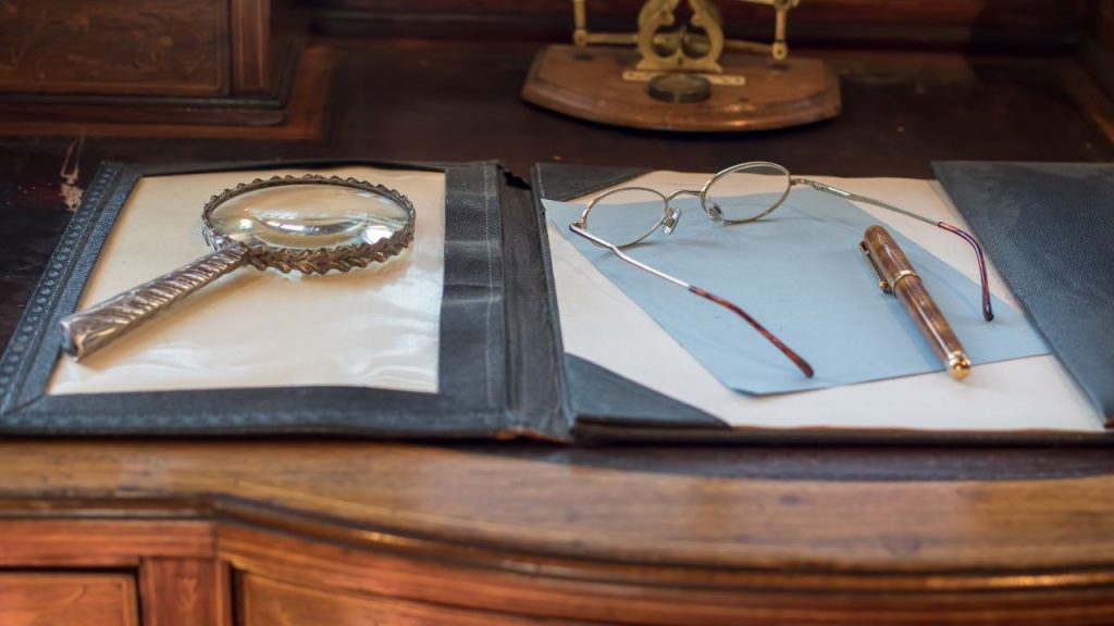 Open folder with a magnifying glass lying on top of the folder to the left and a piece of paper with a pen and glasses lying on top 