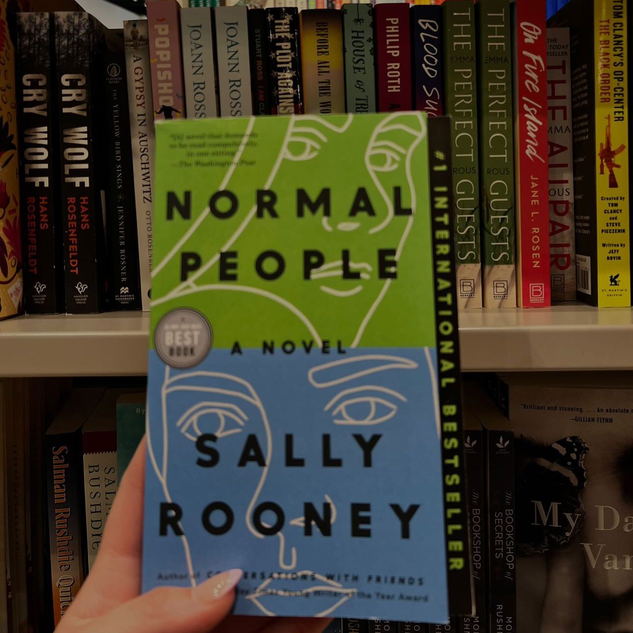 A copy of Normal People being help up in front of library bookshelves