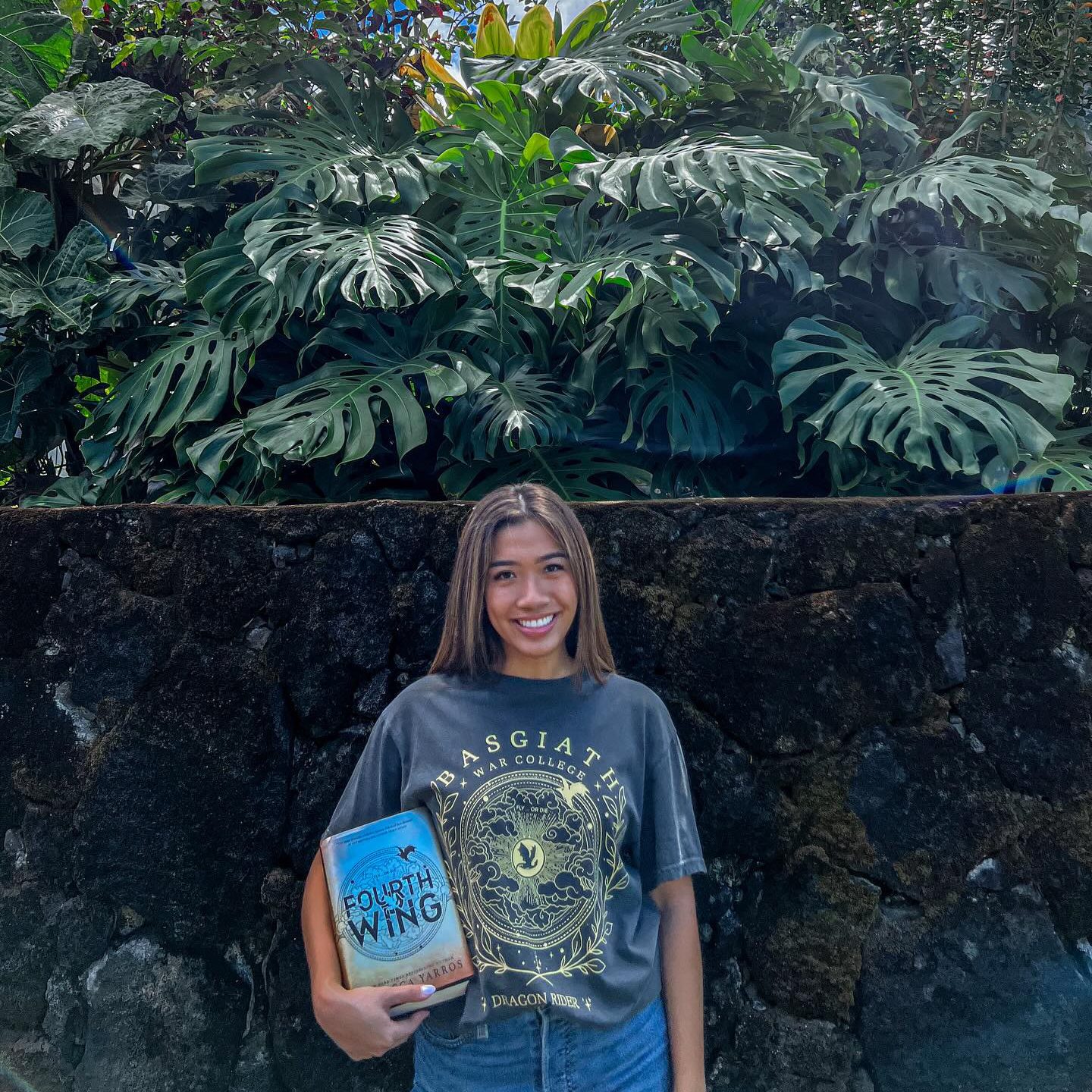 Leira Joyce repping a Basgiath War Collage T-shirt while holding a copy of Fourth Wing