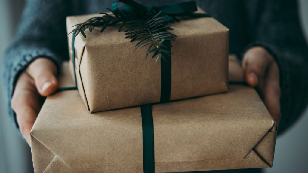 A person holding two presents wrapped in brown paper and green bows.