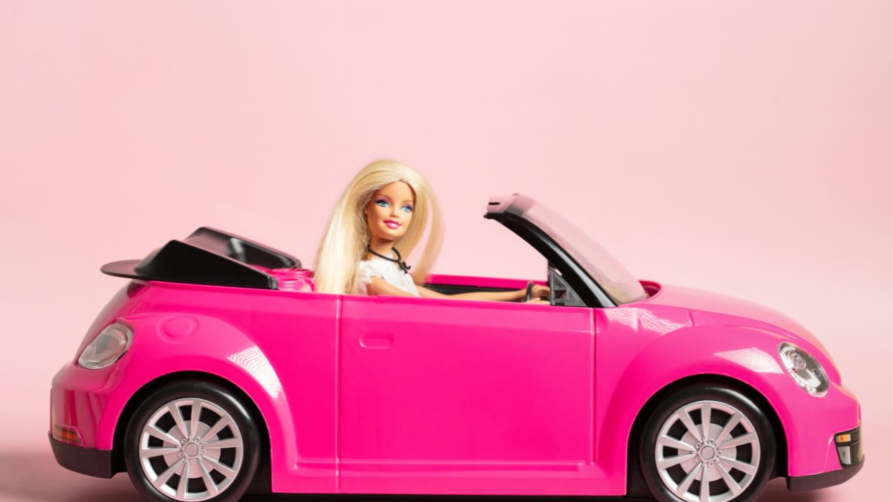 Barbie doll in a pink car set to a pink background