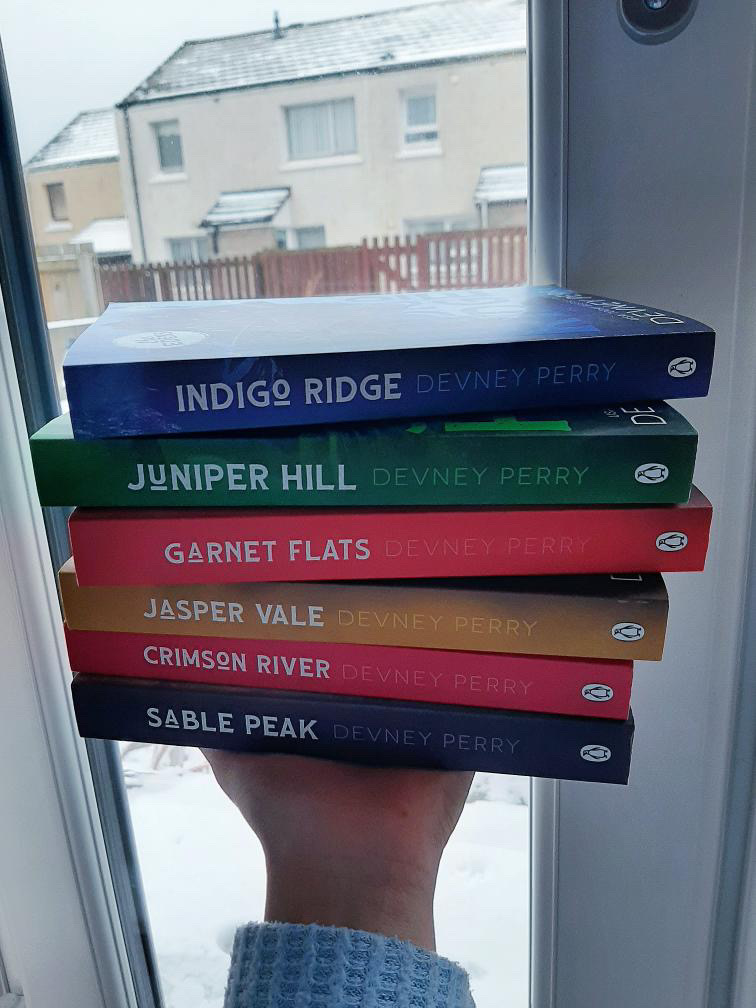 A stack of the Eden Series by Devney Perry being held by Rachel's left hand.