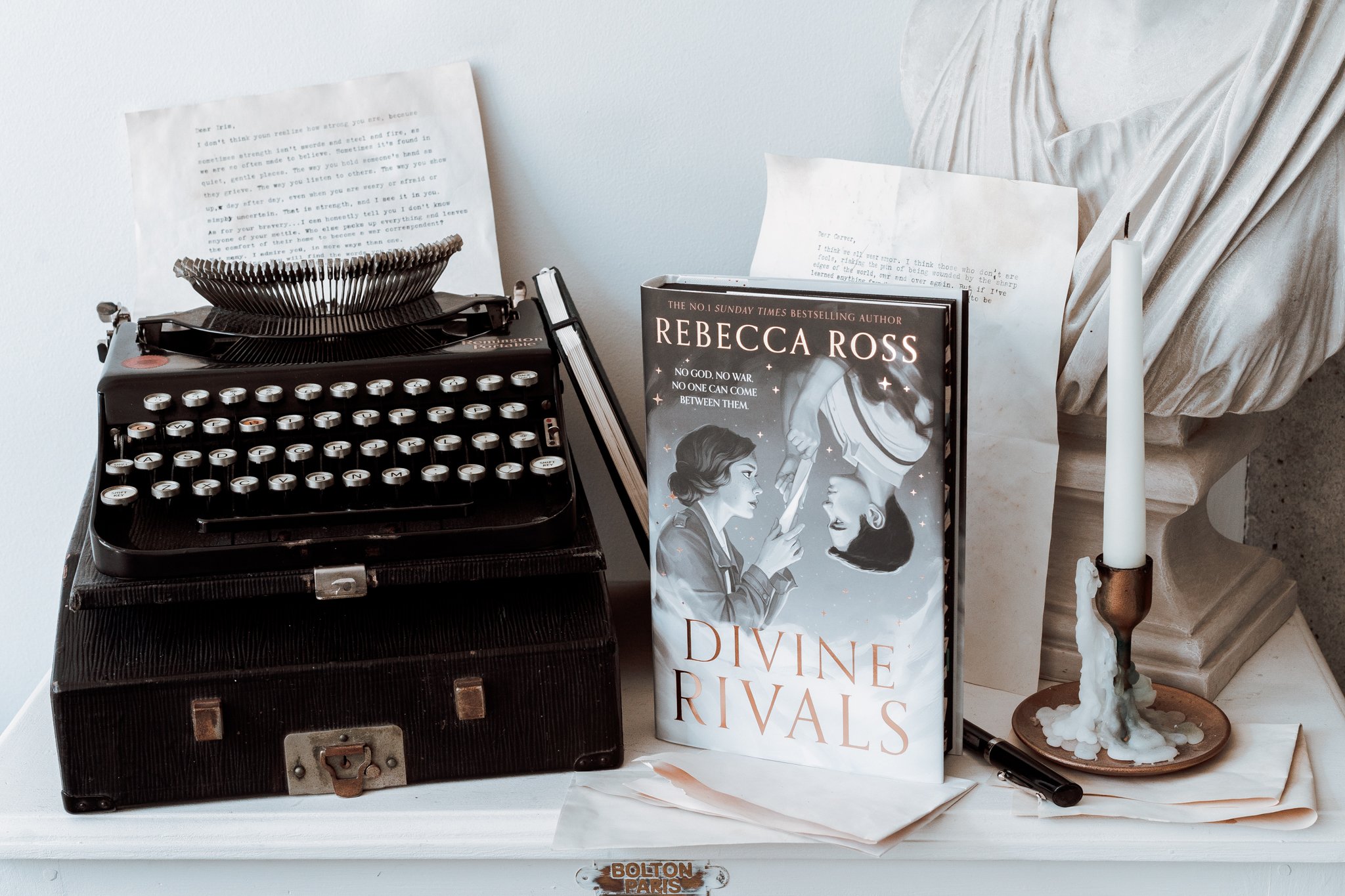 A copy of Divine Rivals stood next to a vintage typewriter on top of a white desk