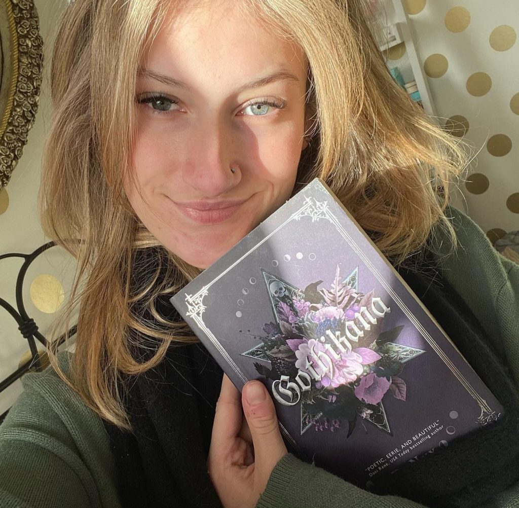 A selfie of Hattie holding a copy of Gothikana by RuNyx