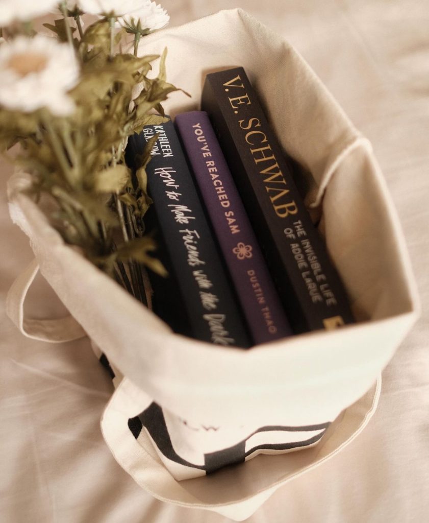 Three book spines seen from inside of a creme tote bag as well as flowers.