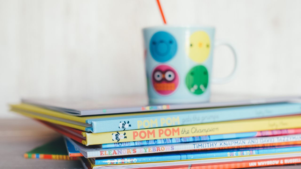 stack of childrens books with a kids cup on top