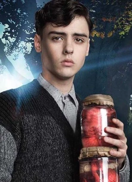 Enoch from the movie Miss Peregrine's wearing a black sweater and holding jars of unknown bodily parts. 