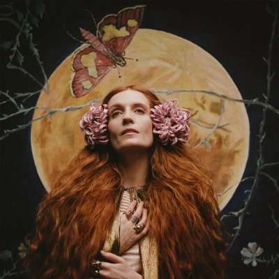 Florence Welch with pink flowers in her hair posing in front of a large yellow moon.