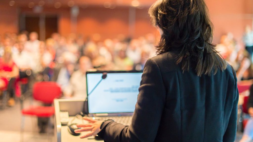 Woman giving a lecture to a large lecture hall.