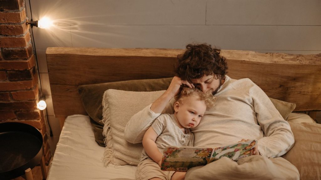 Image of a parent and child in bed reading a book together. 